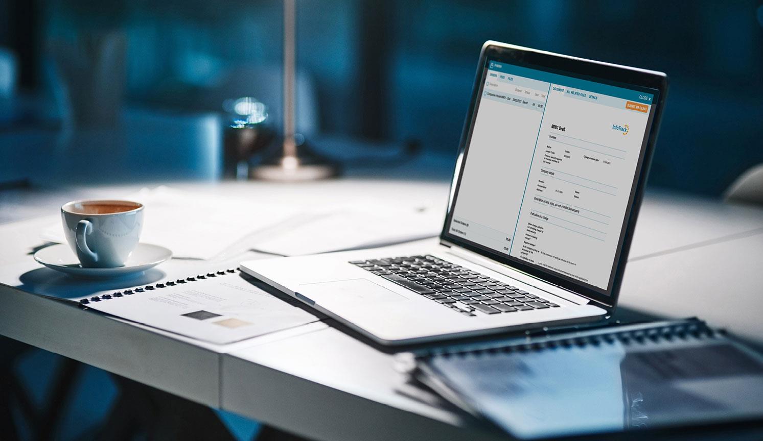 laptop showing InfoTrack software, on a desk at night, surrounded by paperwork and a drained coffee cup